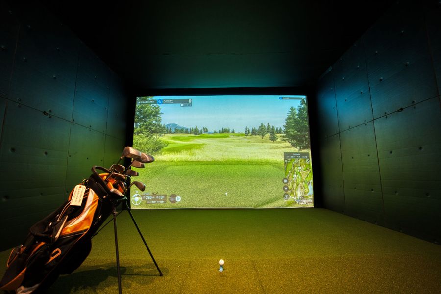 Indoor golf simulator bay with a projection screen and hitting turf